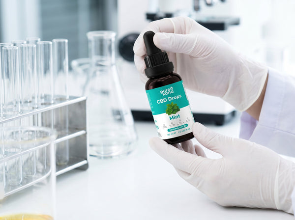 A lab technician holding a PureKana CBD Drops bottle